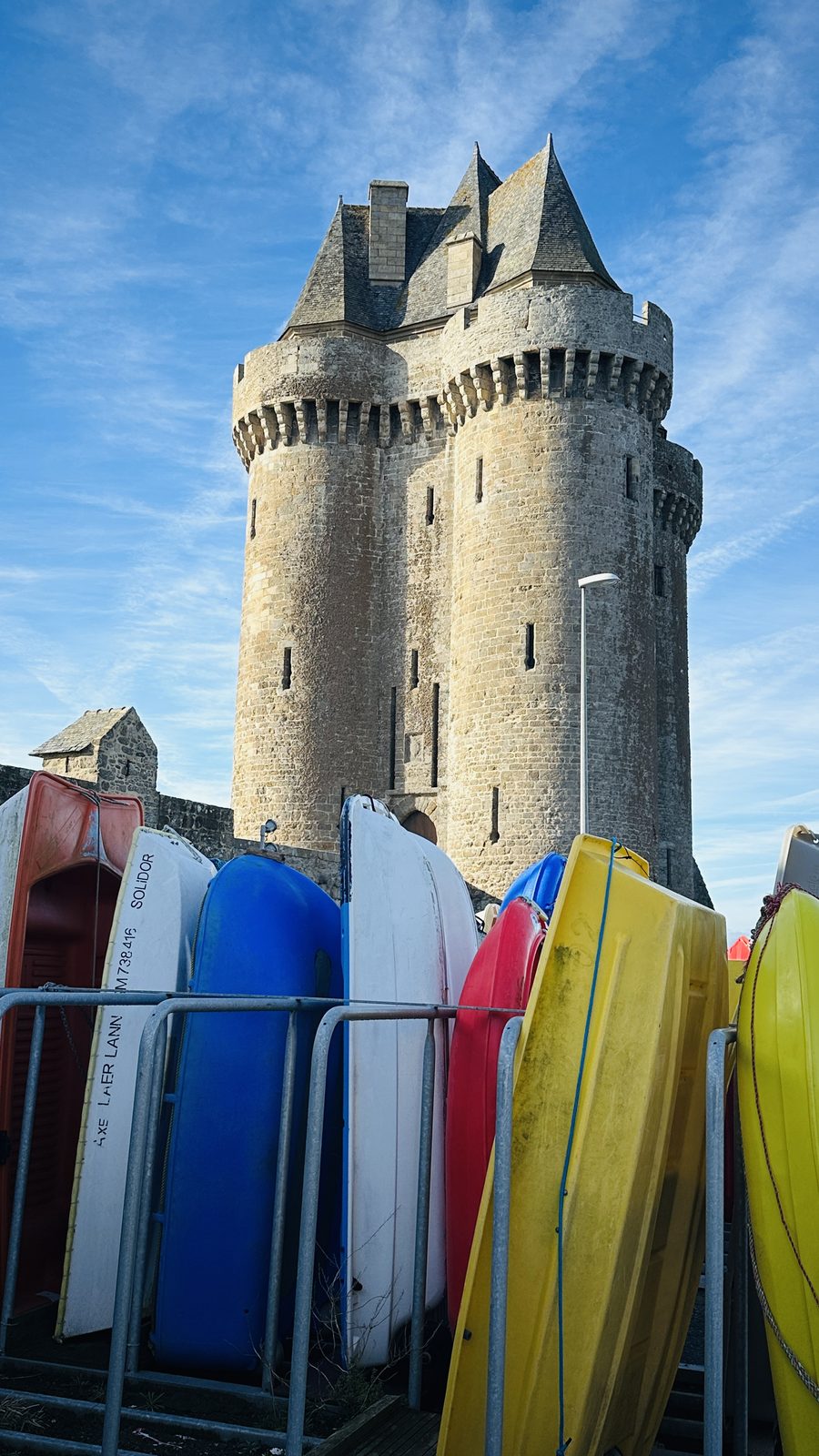 Au pied de la Tour Solidor, les kayaks jaunes, rouges et bleus du club rangés sur leurs racks, sous un ciel bleu.